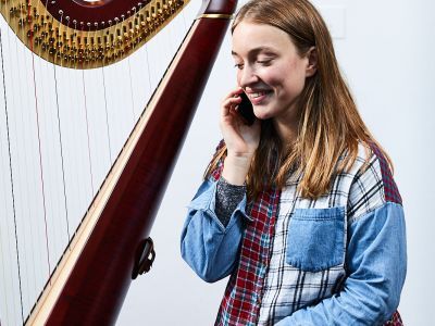 A white woman sits next to a harp, she is on the phone.